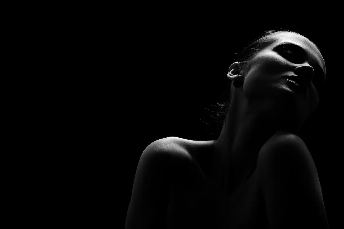 Black and white silhouette of a woman with head tilted back and shoulder exposed against a dark background.