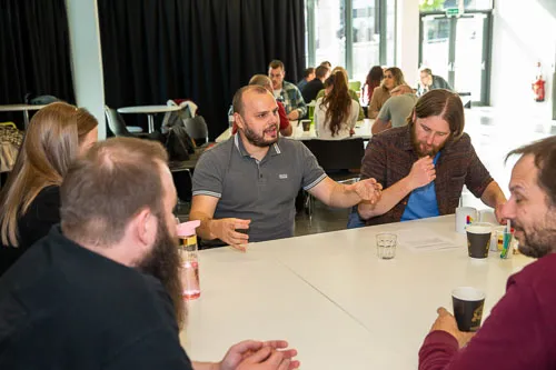 Colleagues gathered around a table, attentively listening to one individual speaking enthusiastically.
