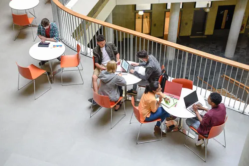A bird's-eye view captures students seated around cafeteria-style tables, engaged in lively conversation.