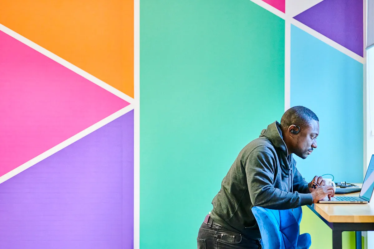 A Leighton colleague working at a standing desk, with a bright and vibrant wall behind him.