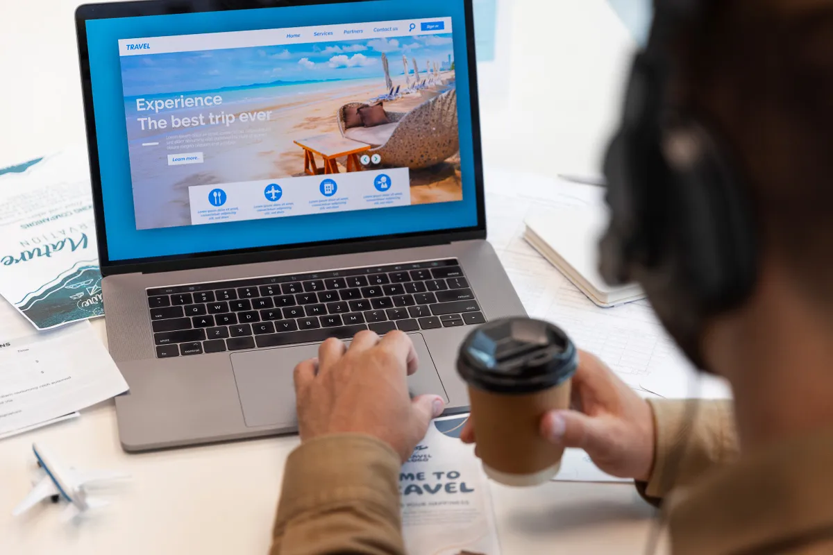 An image of an individual sat at a desk searching for flights on their laptop.