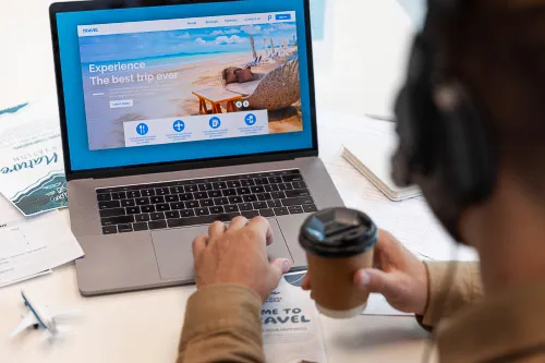 An image of an individual sat at a desk searching for flights on their laptop.
