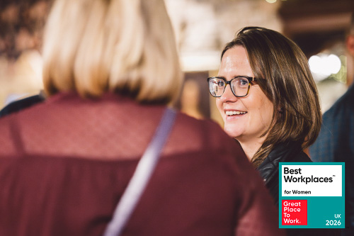 Two Leighton colleagues stood, chatting to one another with the Great Place to Work badge overlaid. 