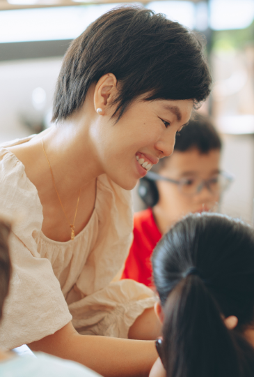 Smiling woman with short hair engaging with children in a bright indoor setting.