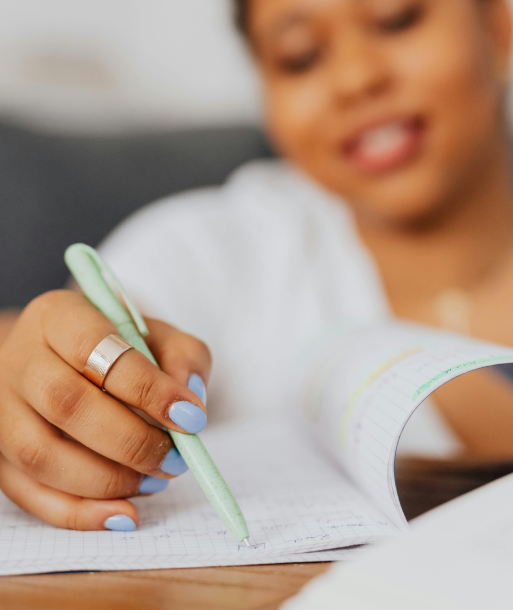 Person with blue nail polish and silver ring writing in a notebook with a green pen.
