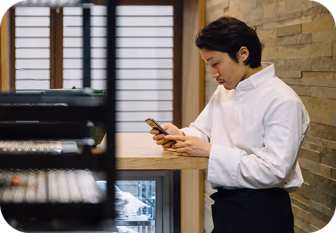 Man in a white shirt looking at his phone while leaning on a wooden counter in a modern room.