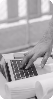 Person's hand typing on a laptop keyboard with a phone and rolled-up papers on the desk nearby.