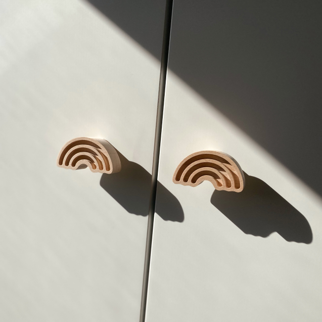 Weiße Schranktüren mit Schrankknäufen die wie zwei Regenbogen aus Holz aussehen.