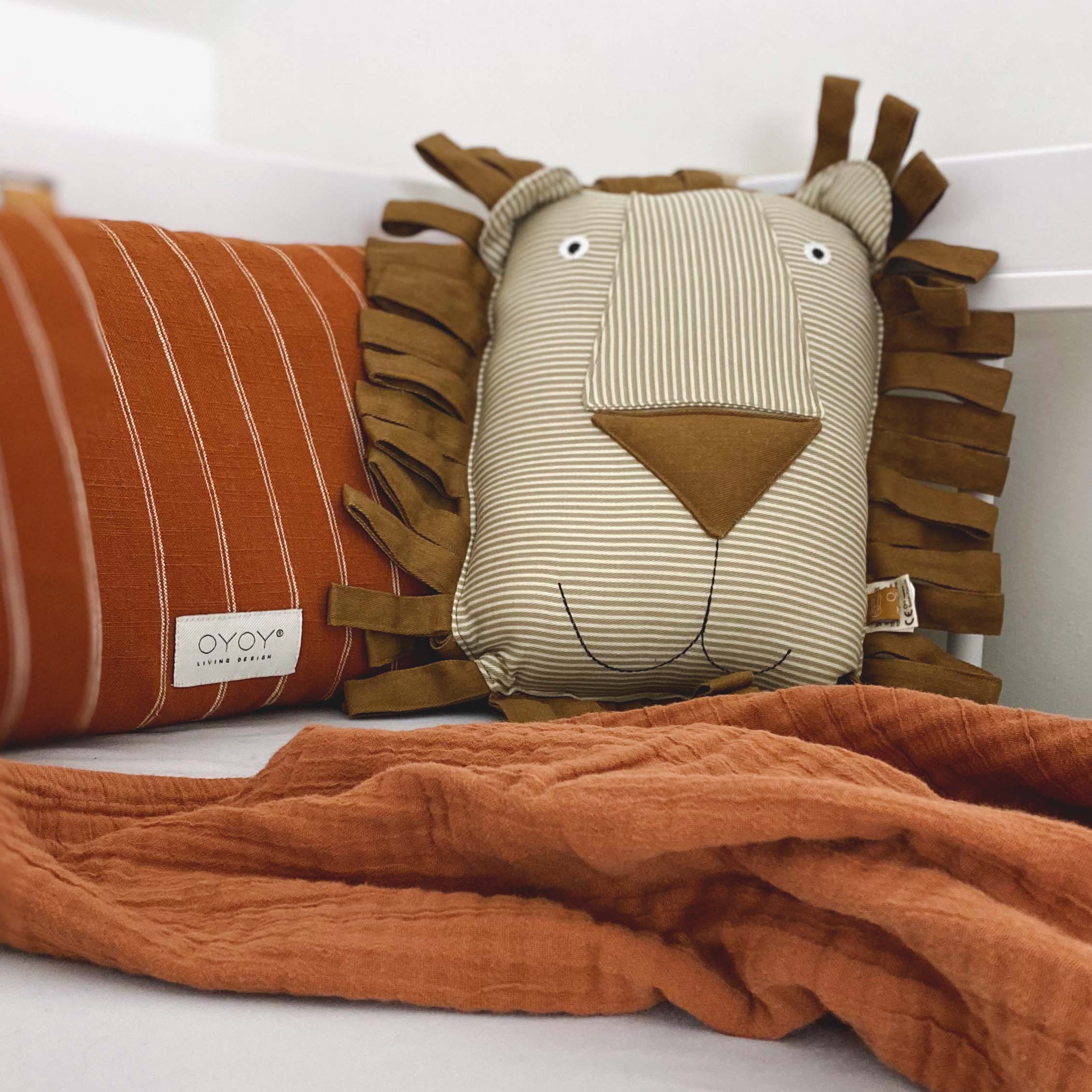 Ausschnitt von einem Kinderbett, mit Fokus auf ein Kissen, dass wie ein Löwengesicht aussieht.