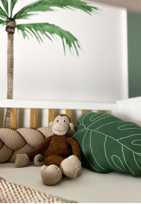 Ein Stofftier-Affe neben einem Blattkissen auf einem Kinderbett.