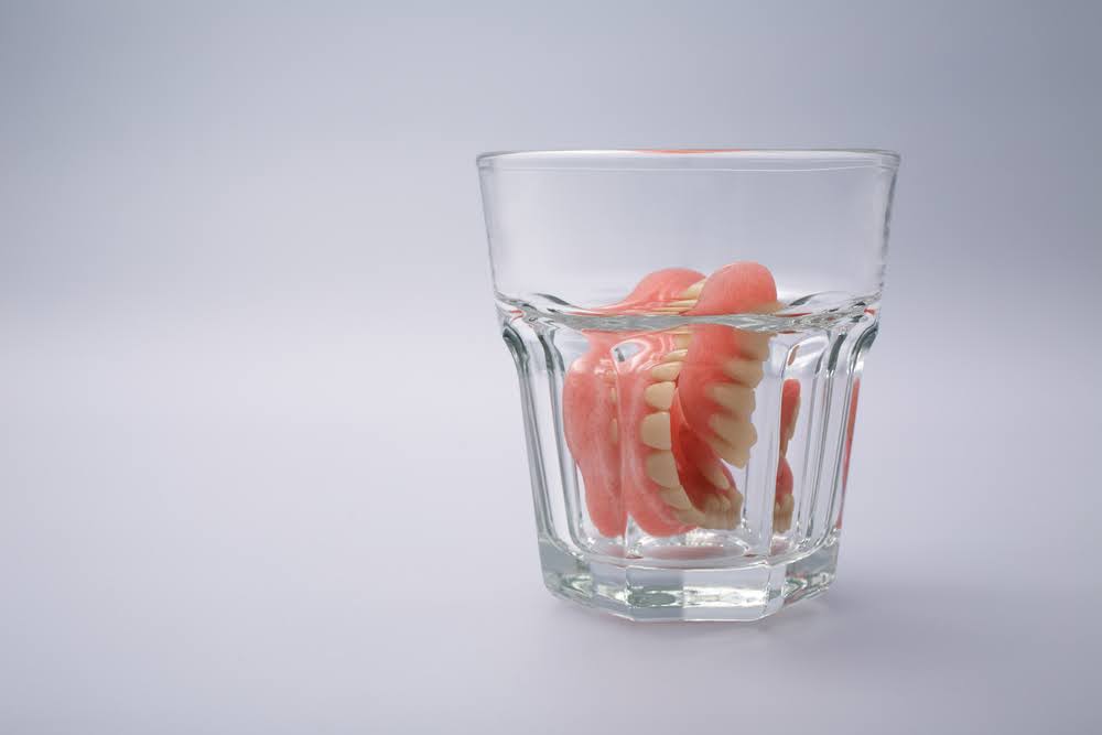 dentures being stored in a glass of denture cleaning solution or water