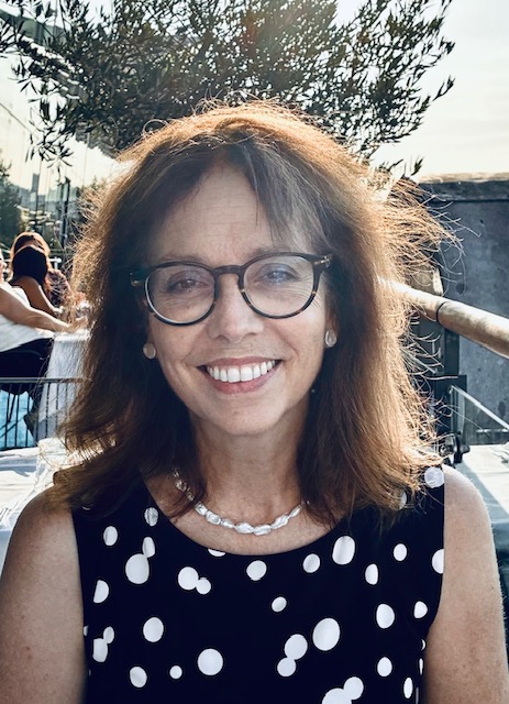 A smiling woman in a polka-dotted shirt wearing glasses