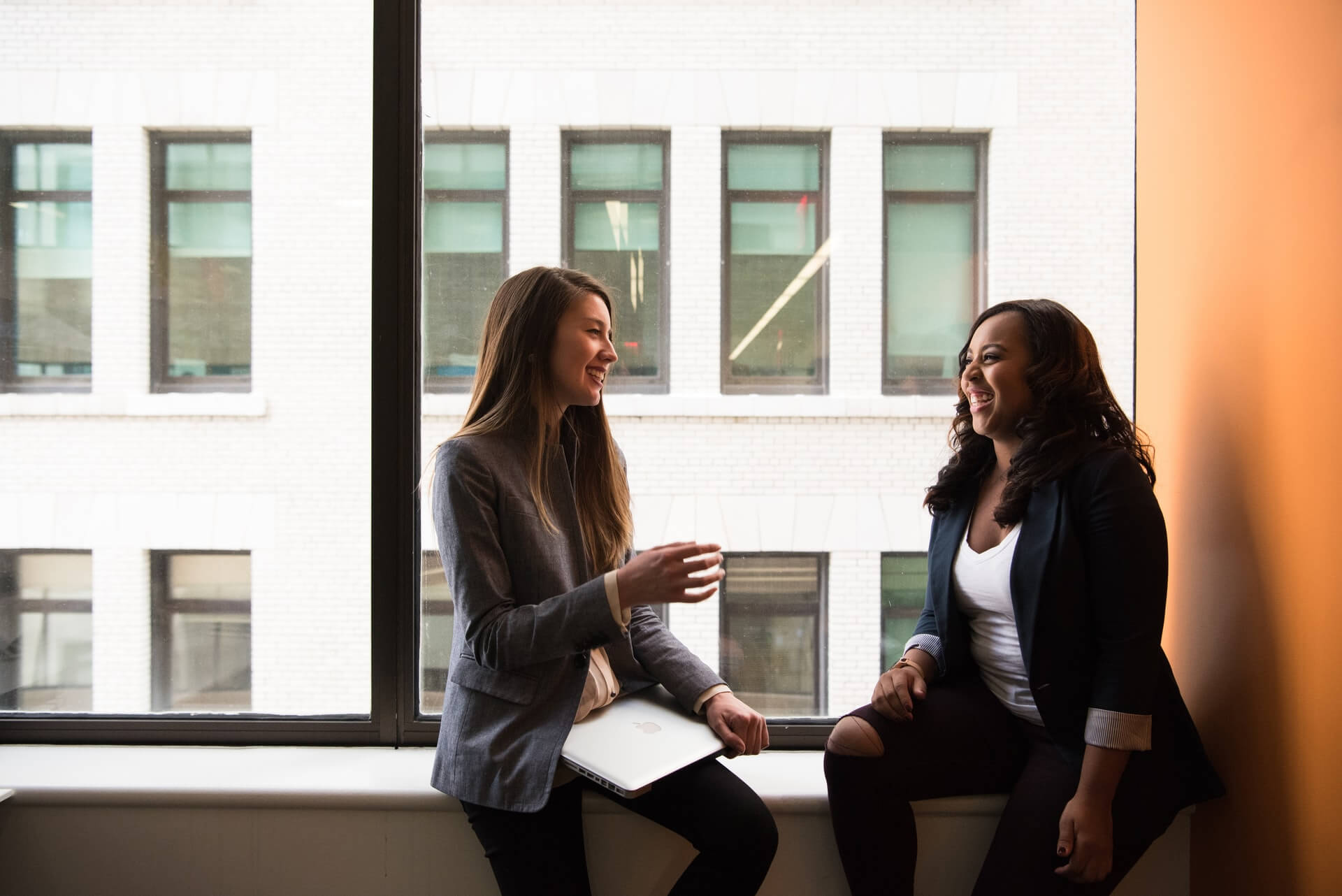 two woman sitting by the window laughing