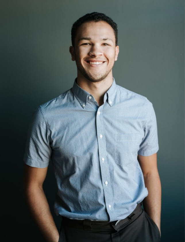 smiling man wearing blue and white gingham button-up collared shirt putting his hands on his pocket