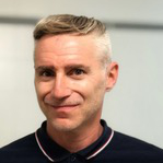 Michael Woditschka, Smiling man with short, light-colored hair and wearing a dark polo shirt with a red and white collar.