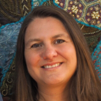 Ruth Byrne, Autorin, Smiling woman with long brown hair in front of a colorful fabric background.