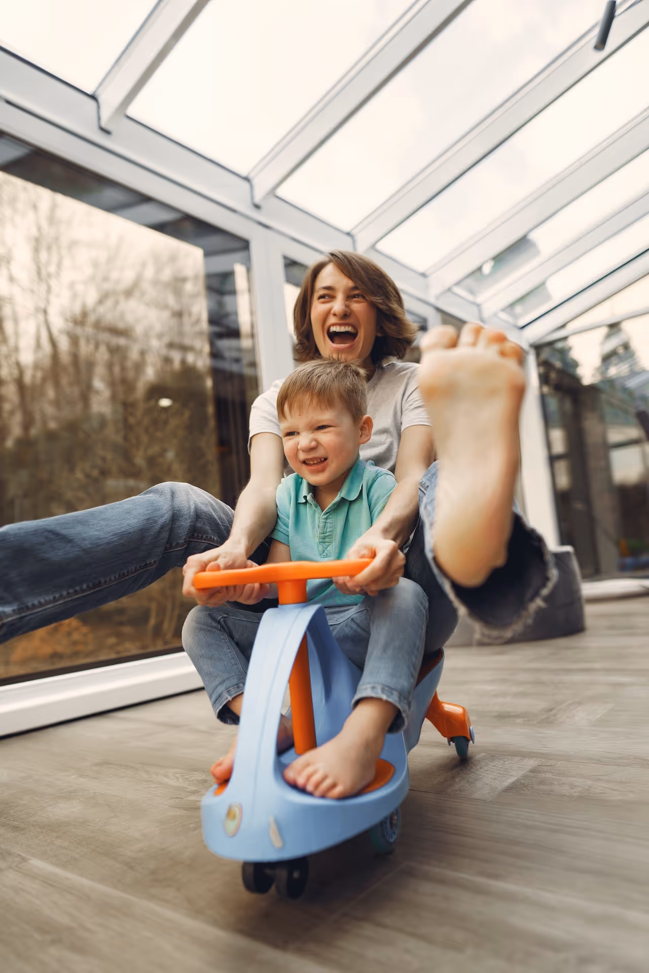 mother_riding_kids_scooter_toy_with_young_son_looking_happy