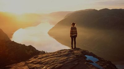 A person standing on a rock overlooking a river and watching the sun rise.