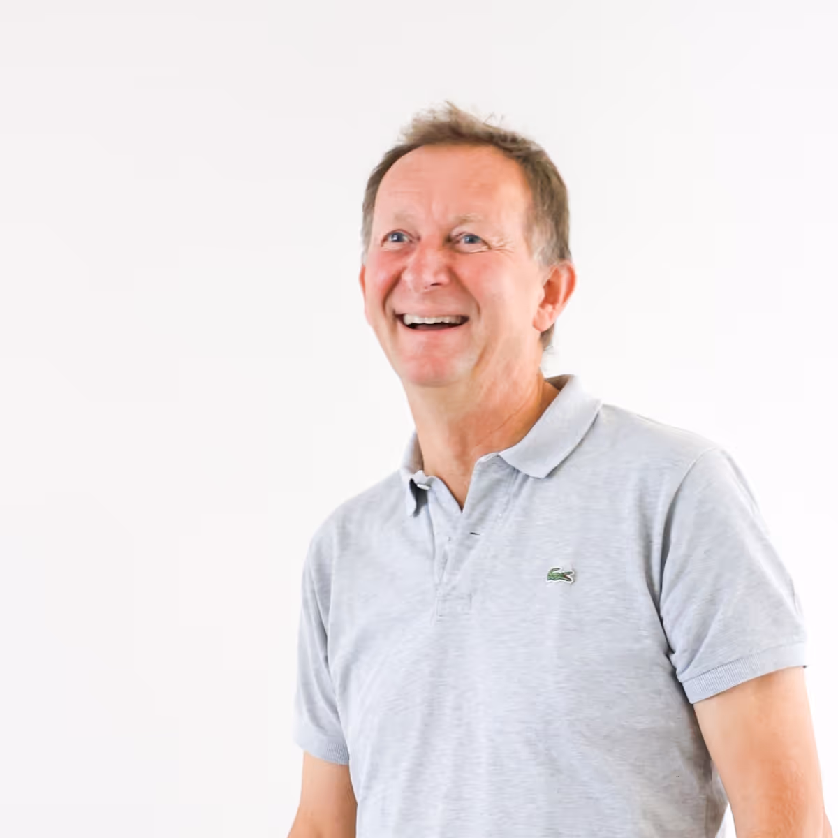 Lachende man in een lichtgrijs poloshirt tegen een witte achtergrond.