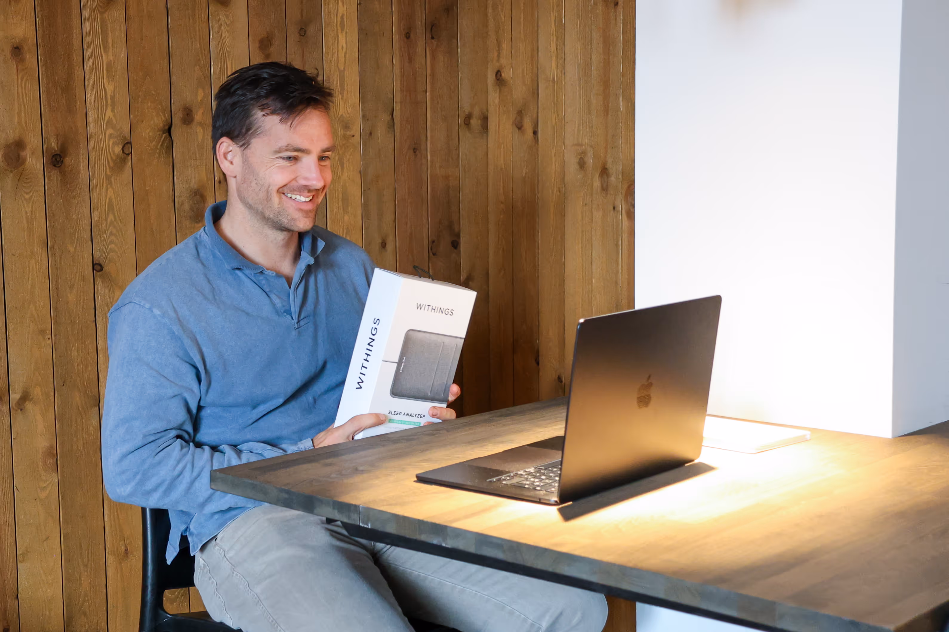 Man zit aan tafel met laptop en houdt een doos vast van een Withings Sleep analyzer.