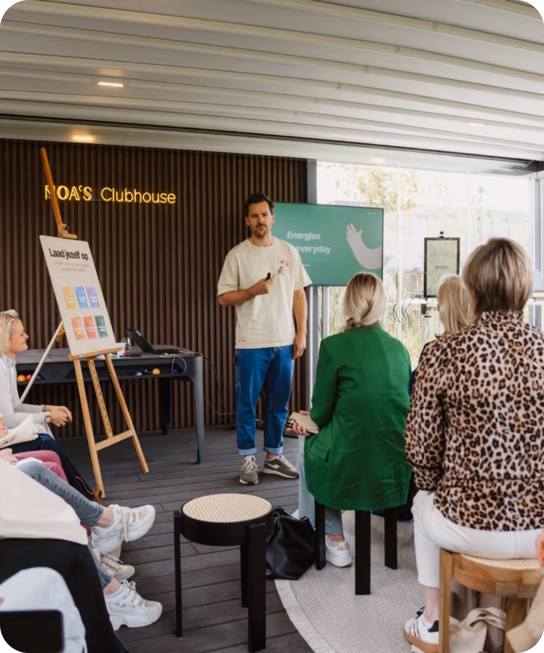 Man geeft presentatie aan zittend publiek in een moderne ruimte met scherm en whiteboard.