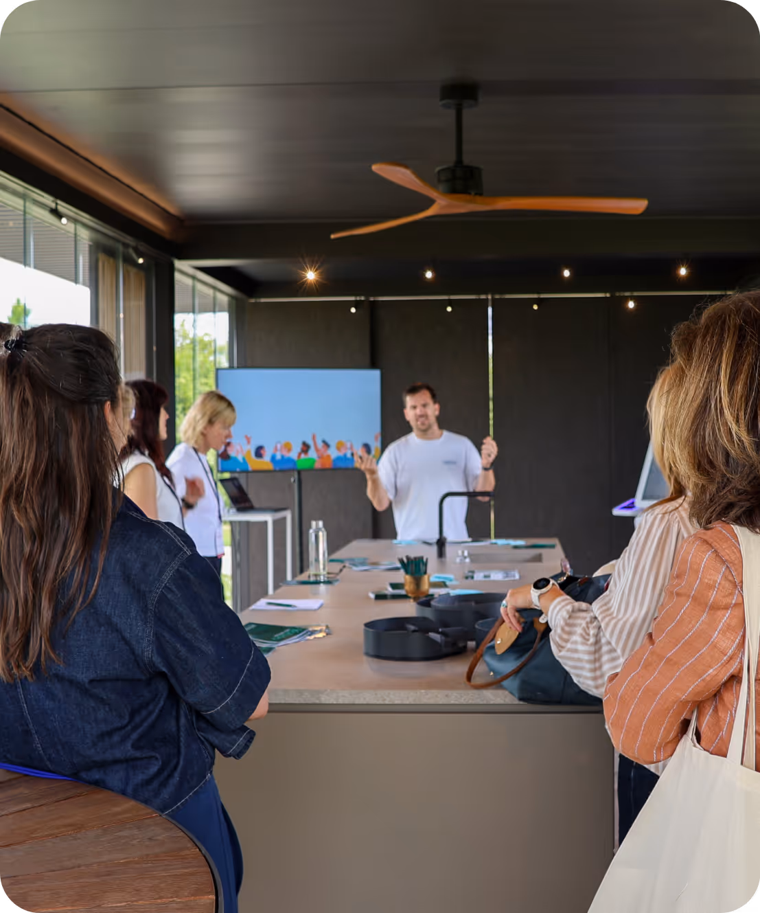 Man geeft een presentatie aan een groep mensen rond een tafel in een moderne vergaderruimte.