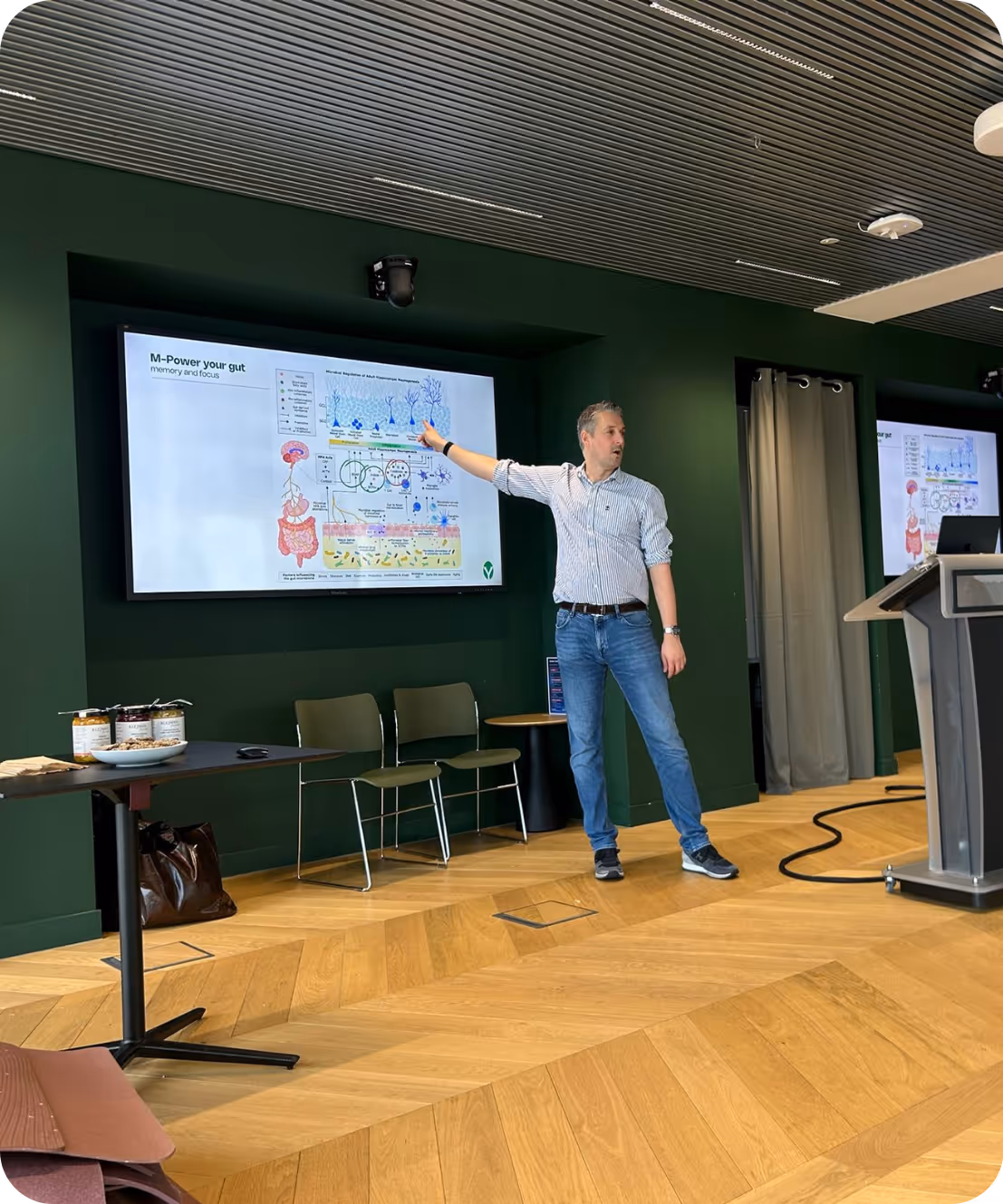 Man wijst op een scherm met een diagram over darmgezondheid in een groene vergaderruimte.