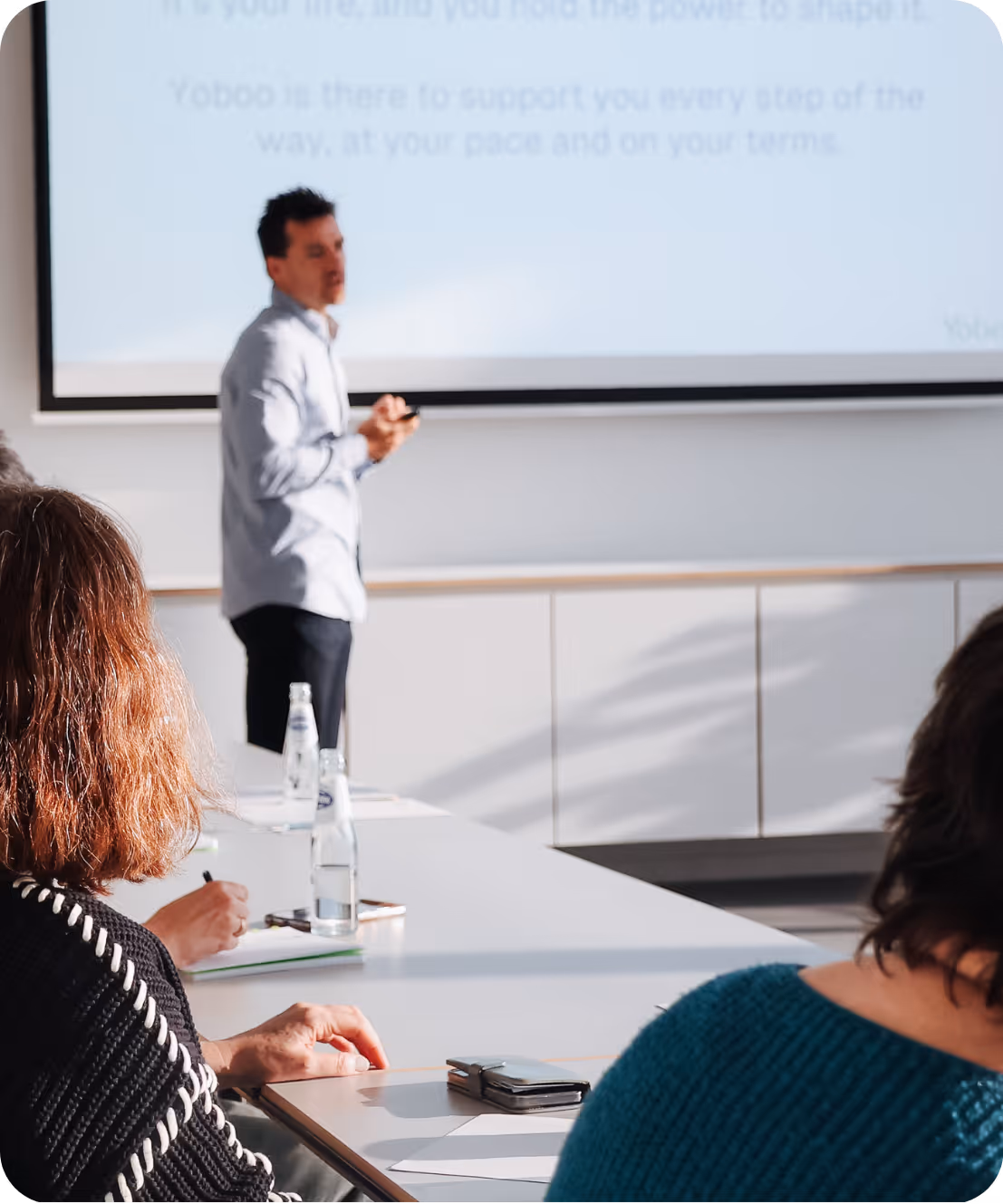 Man giving a presentation to seated people taking notes in a bright conference room.