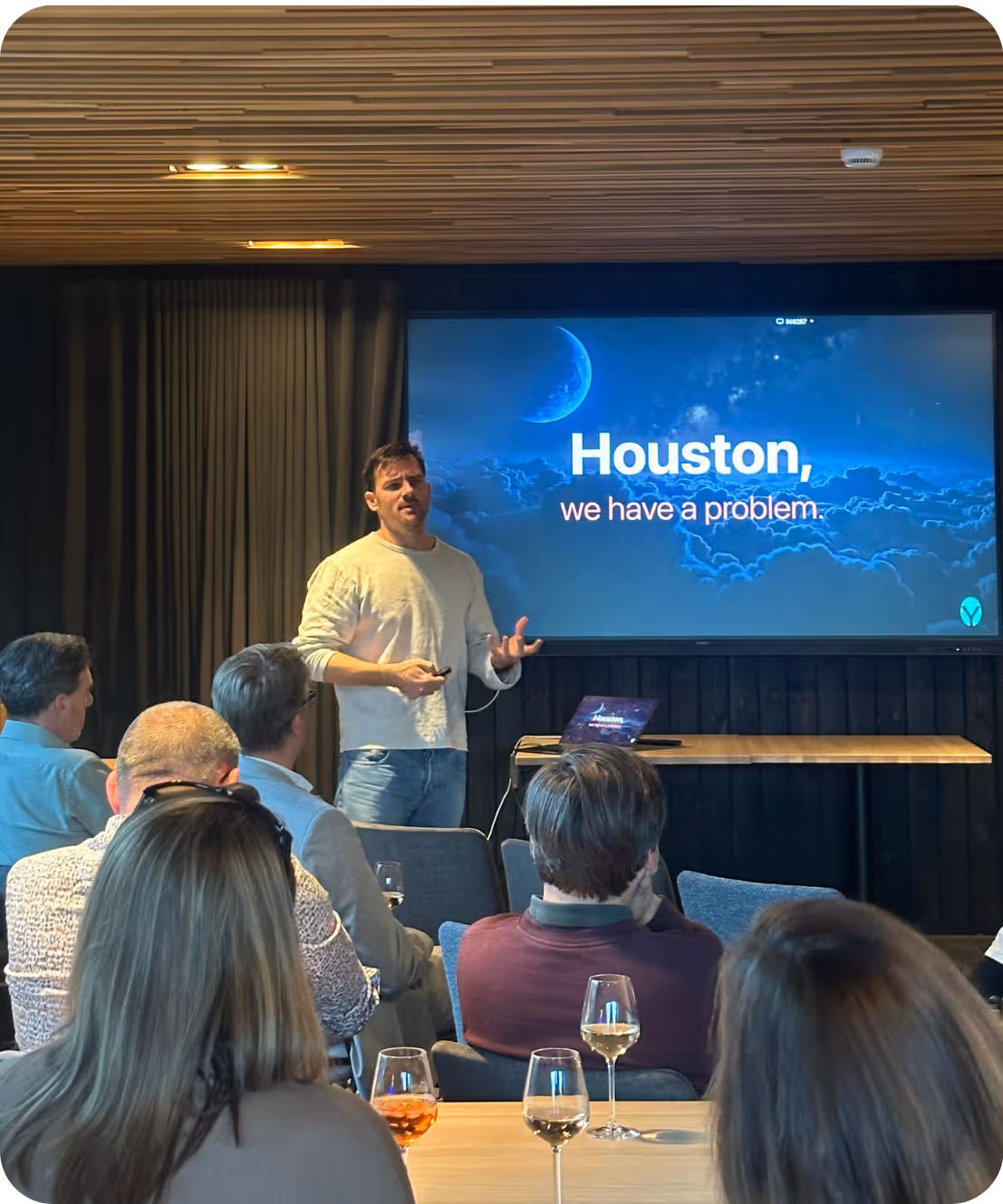 Man geeft presentatie aan publiek; scherm toont tekst: Houston, we have a problem.