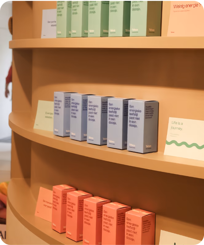 Rekken met drie niveaus van kleine doosjes in groene, blauwe en rode tinten, elk met de tekst 'Een energieke leefstijl past niet in een doosje' in het Nederlands, en een kaartje met de tekst 'Life is a journey.'