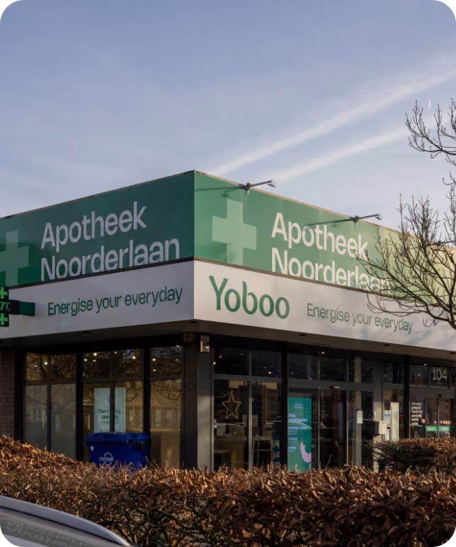 Hoek van een gebouw met groene borden waarop 'Apotheek Noorderlaan' staat, met het logo van een kruis, en daaronder een witte strook met de tekst 'Yoboo Energise your everyday'.