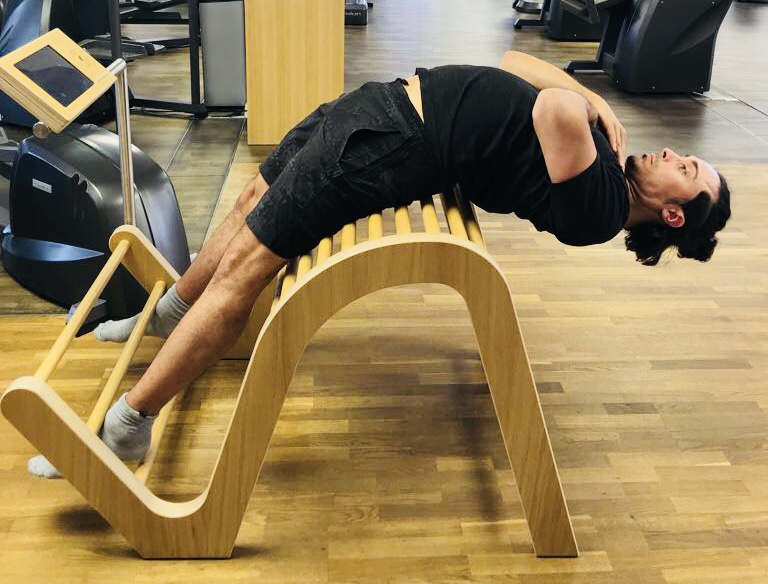 Uomo in estensione della colonna su panca curva durante pratica di Biokinematik