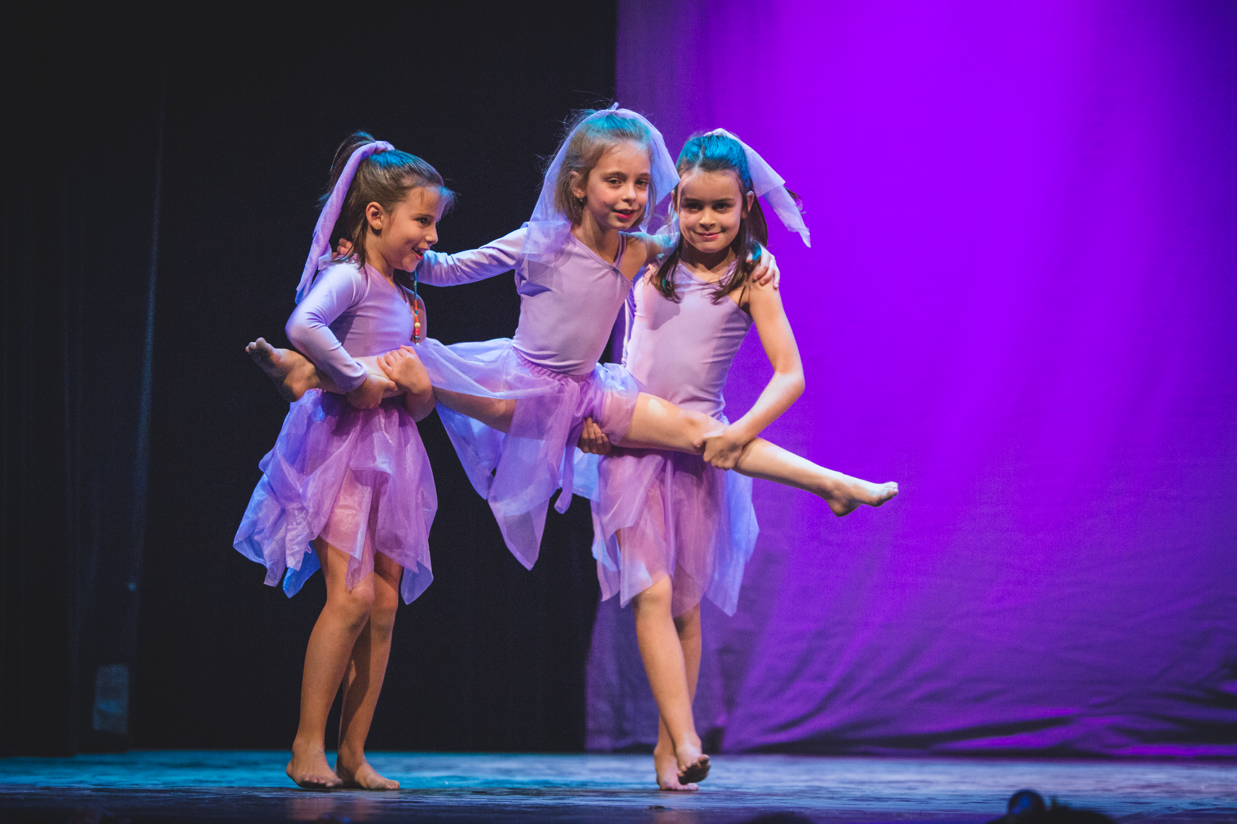 Esibizione sul palco con bambine in costumi lilla sotto luci viola