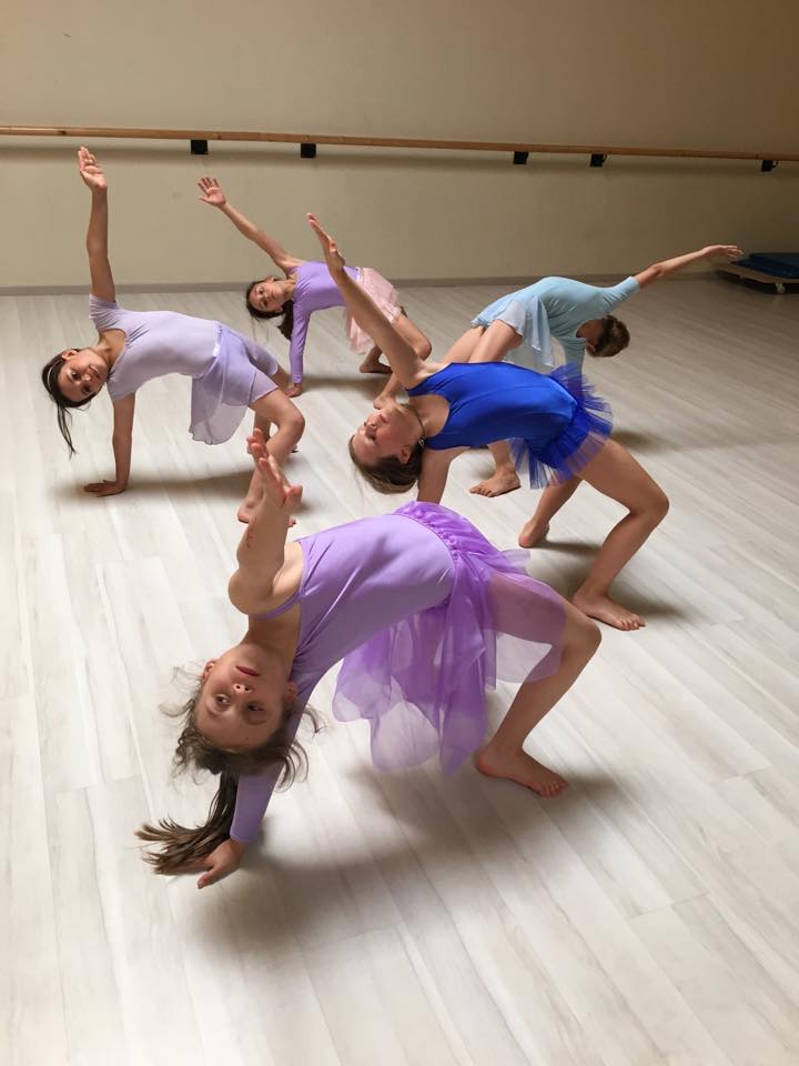 Bambine in abiti di danza eseguono coreografia di gruppo sul parquet della sala danza