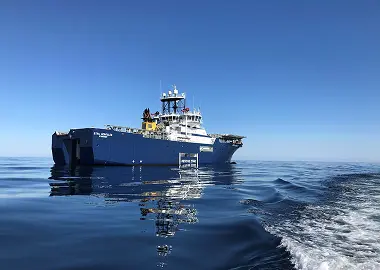 Blue offshore support vessel “Stril Herkules” on a calm, glassy sea under a clear sky, with a visible “RESCUE ZONE” marking on the hull.