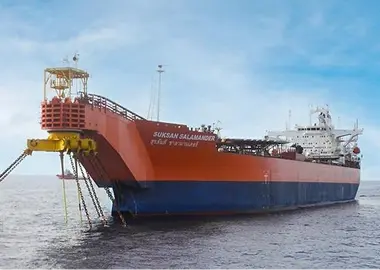 Bow-quarter view of an orange-and-blue FPSO/FSO named Suksan Salamander, turret-moored with anchor chains leading forward on calm water beneath a clear sky.
