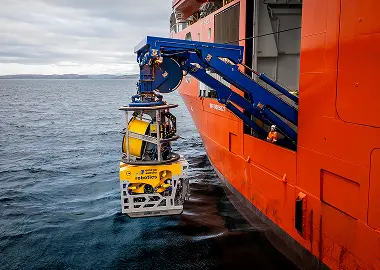 Remotely operated underwater vehicle being launched from an orange offshore vessel into the sea.