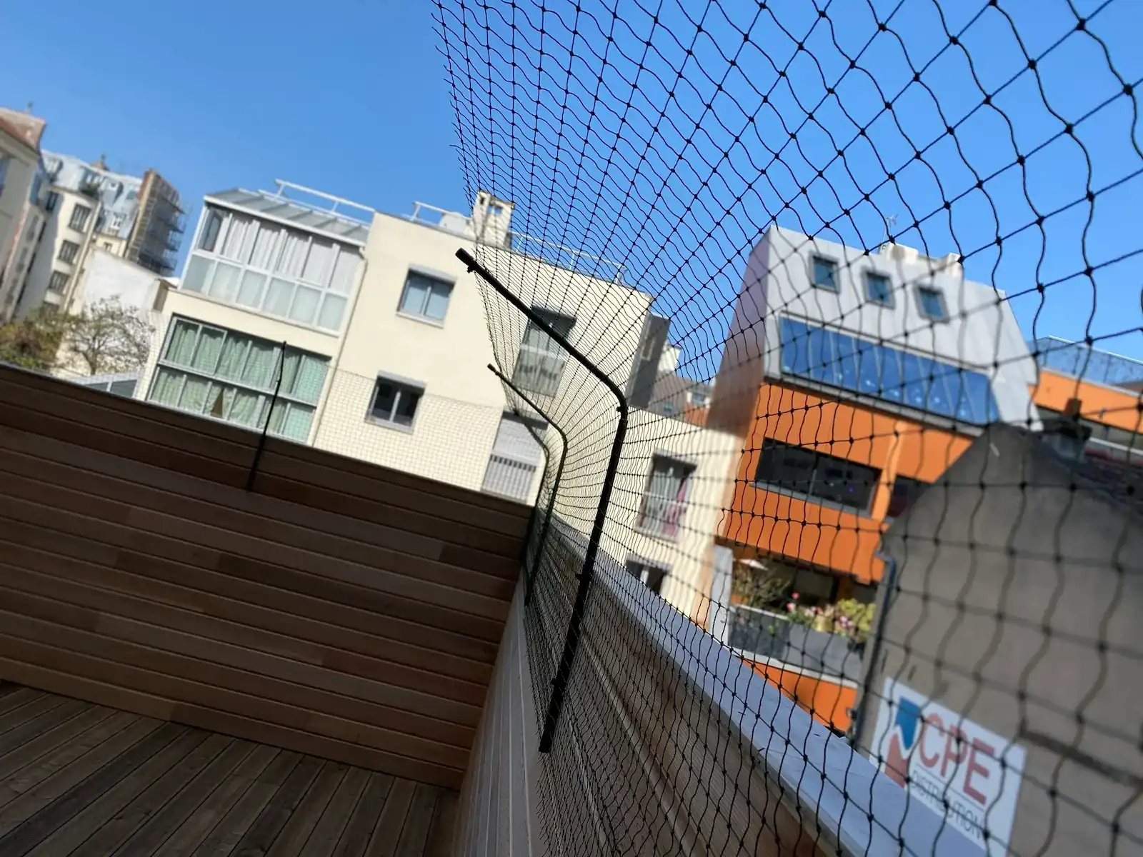 Balcon avec garde-corps en bois et filet de protection, vue sur des immeubles résidentiels sous ciel bleu.