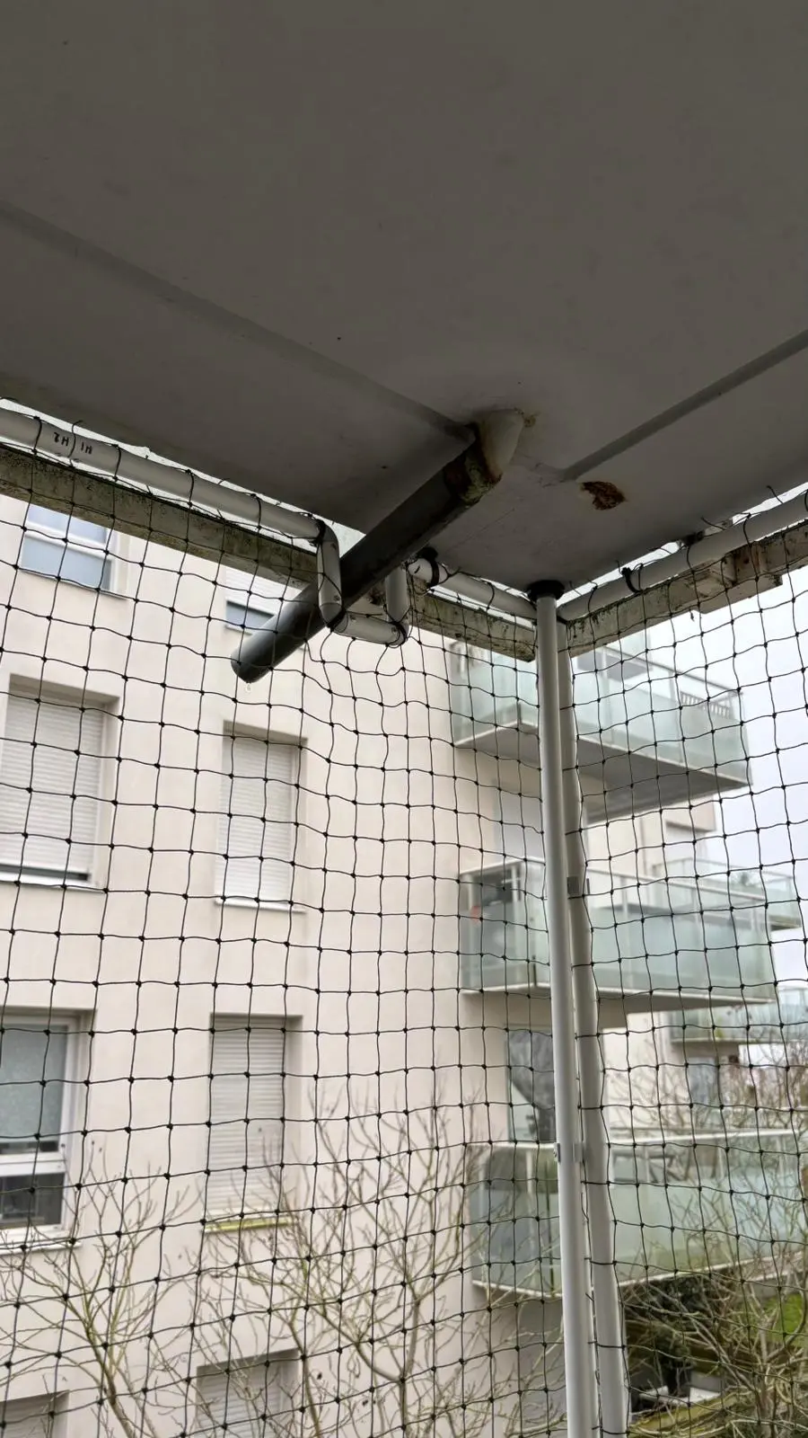 Vue d'un balcon protégé par un filet de sécurité avec un bâtiment résidentiel en arrière-plan.