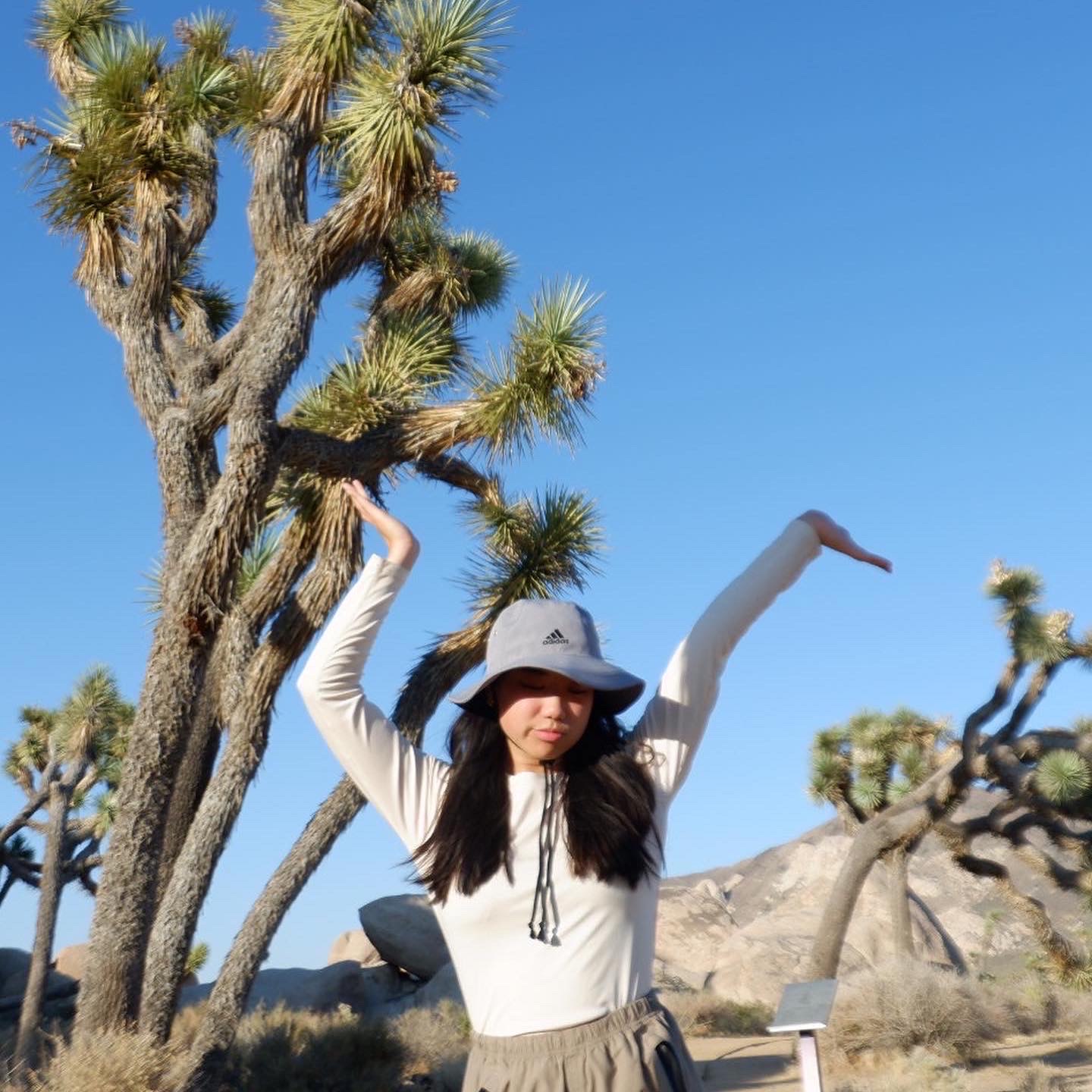 Lydia in front of a Joshua Tree, holding hands up.

