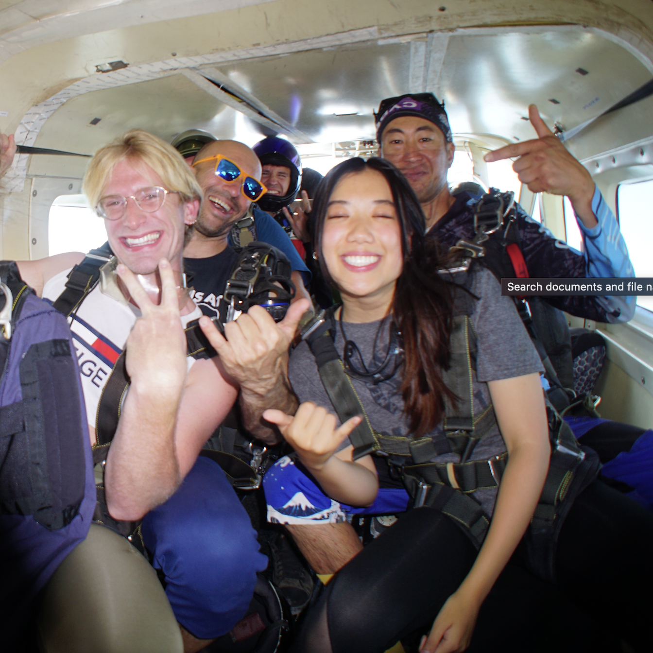 Lydia holding up swing loose sign with hands, on a plane for skydiving with others.
