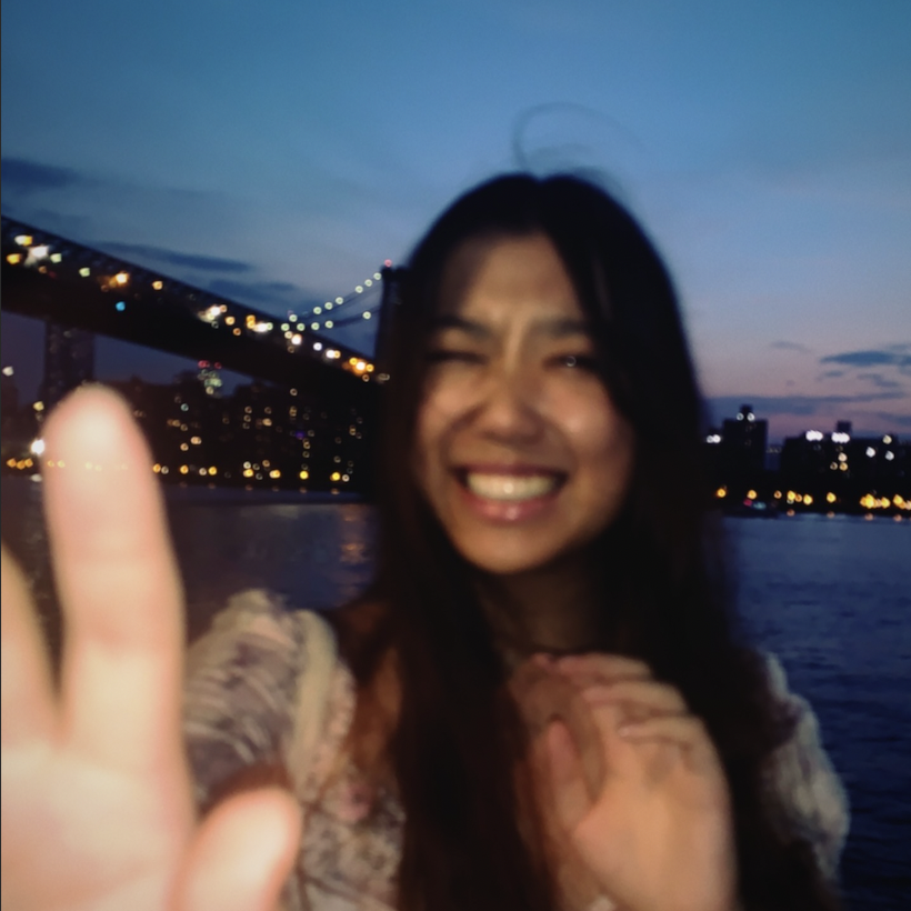 Lydia smiling and reaching for camera in front of Brooklyn Bridge, New York.

