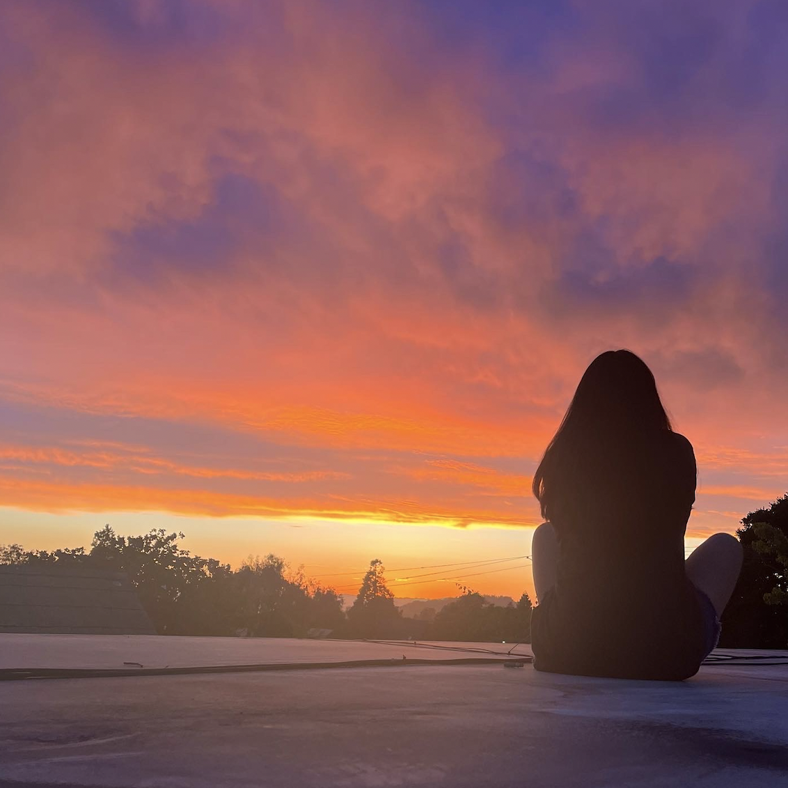 Lydia sitting facing a beautiful 
sunset.