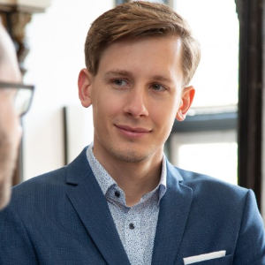 Kundentestimonial: Junger Mann im blauen Anzug lächelt leicht und blickt aufmerksam auf sein Gegenüber.