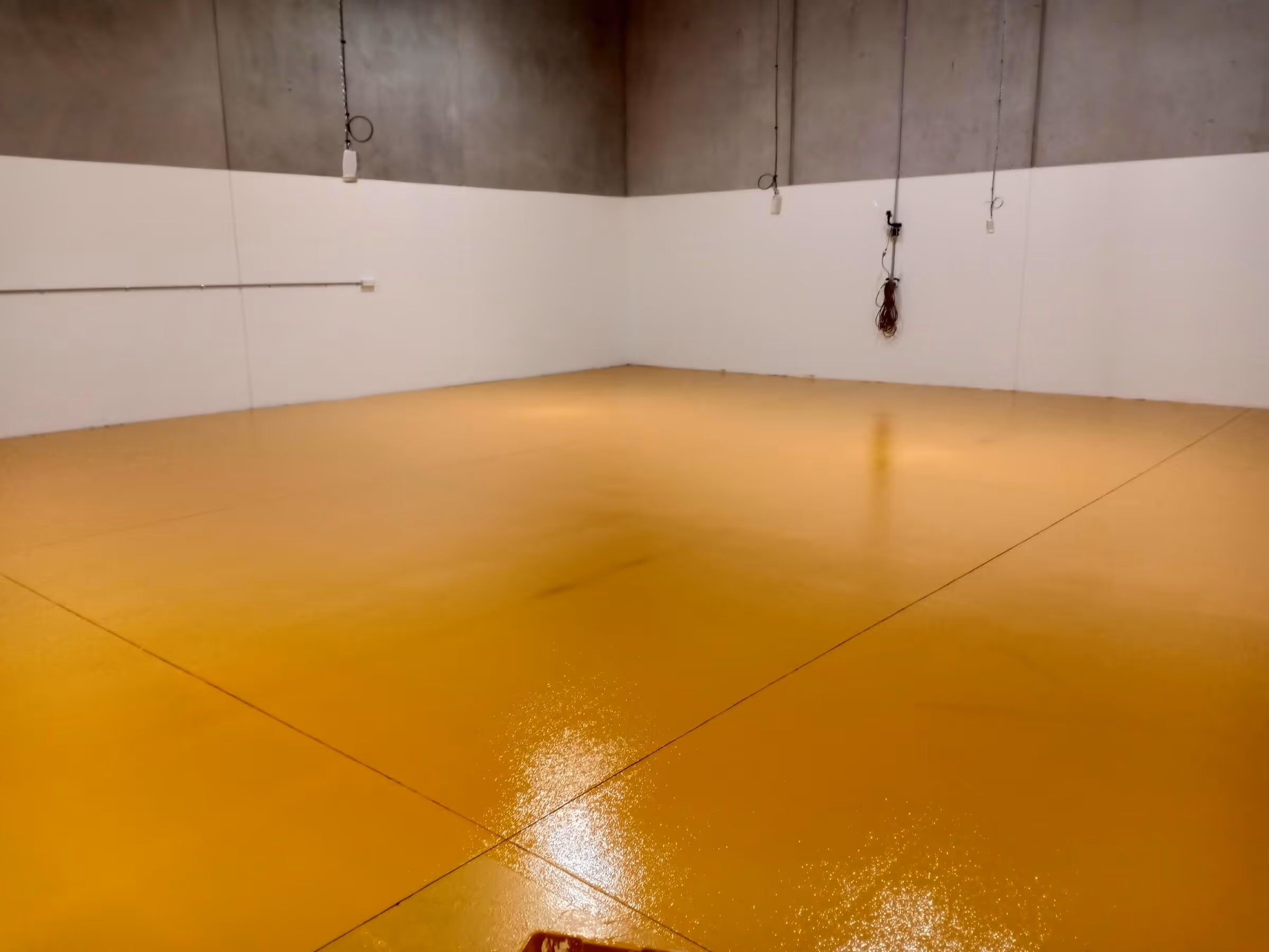 Empty industrial room with glossy yellow epoxy floor and white lower walls with concrete upper walls.