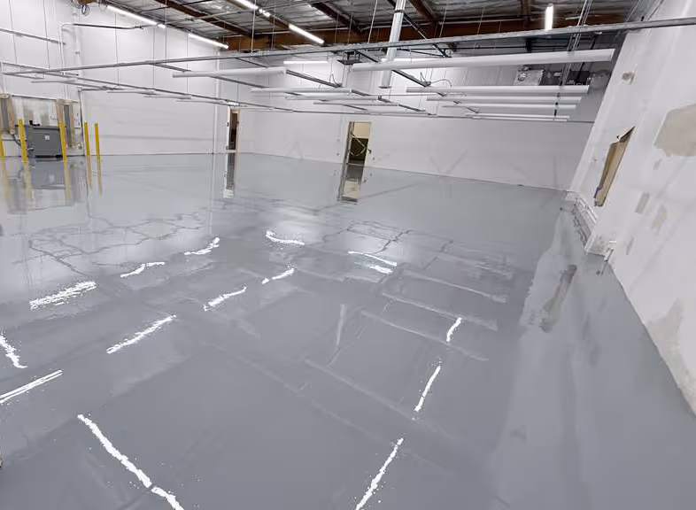 Empty industrial warehouse space with smooth, glossy light gray epoxy floor and white walls.