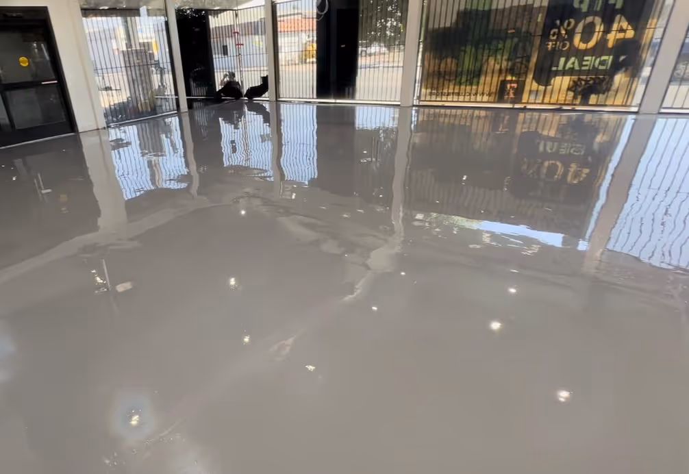 Shiny, smooth light gray commercial epoxy floor in a large room with windows reflecting outdoors.