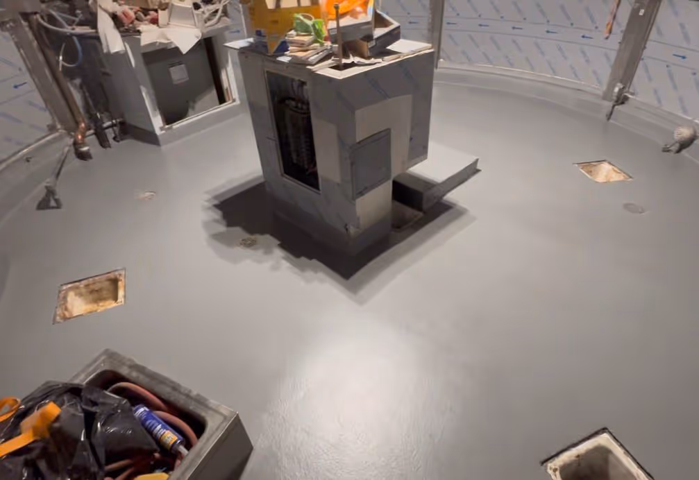 Industrial or lab room with smooth gray urethane cement floor and central equipment covered with protective panels.