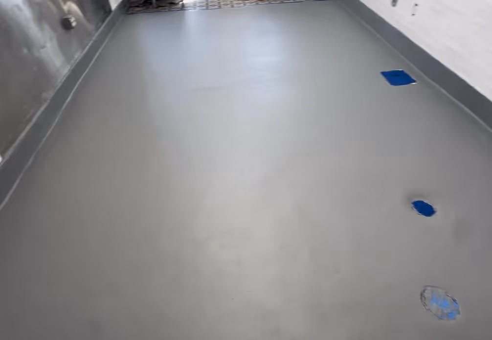 Smooth gray commercial urethane-coated cement floor with three blue floor drains along the right side.