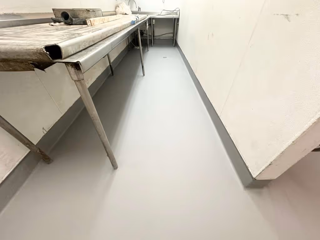 Long industrial workspace with smooth light gray urethane cement floor and metal tables along the wall.